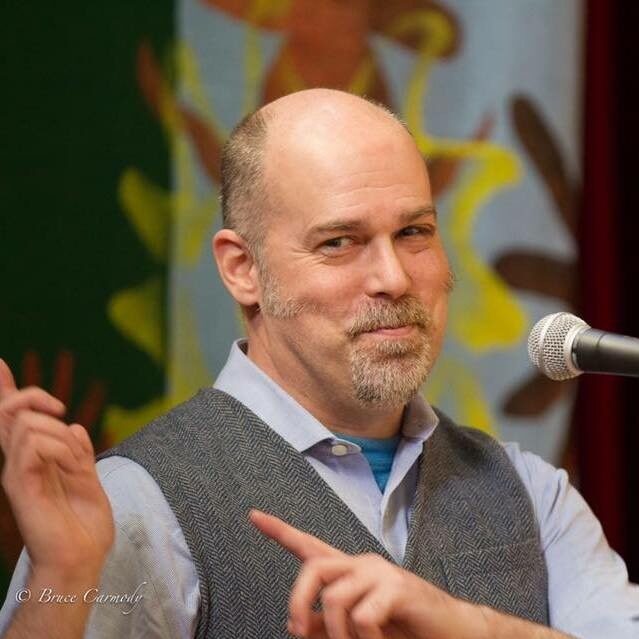A man speaking into a microphone with a confident expression.